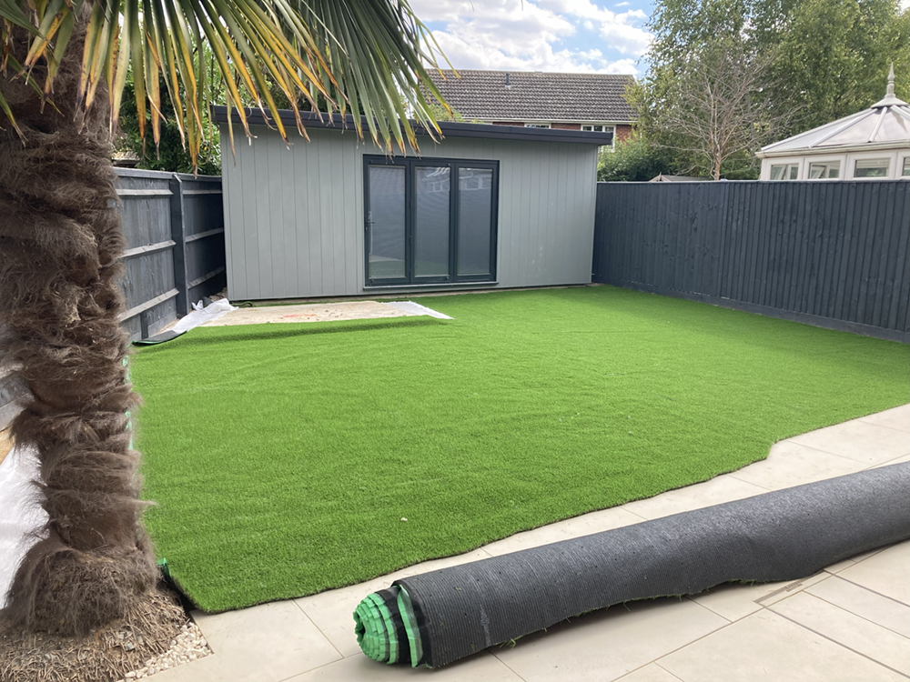 Artificial turf lawn with grey garden office and sandstone patio edging